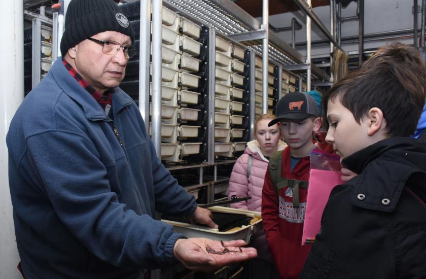 Hatchery specialist holds coho salmon alevins as children gather around