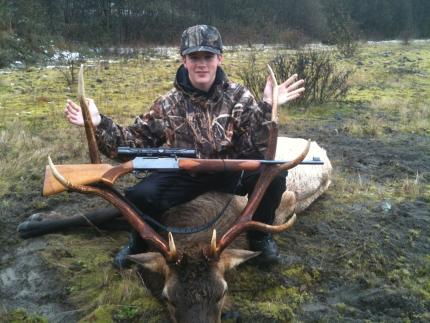 Young hunter with harvested elk. Scoped rifle sitting across antlers to show size of rack.