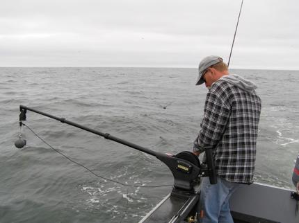 A fisherman standing next to manual downrigger with a cannon ball attached to the line.