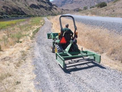 An employee smoothing out a rock path with a tractor