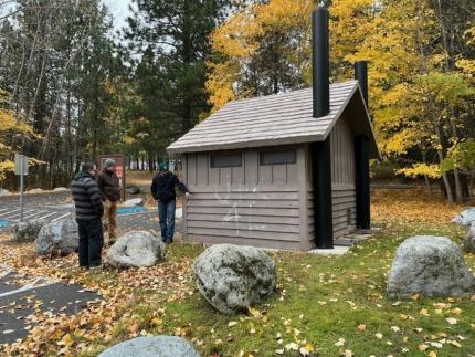 Three people looking at some recently cleaned graffiti on a small building. 