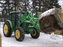 A green tractor moving a haybale